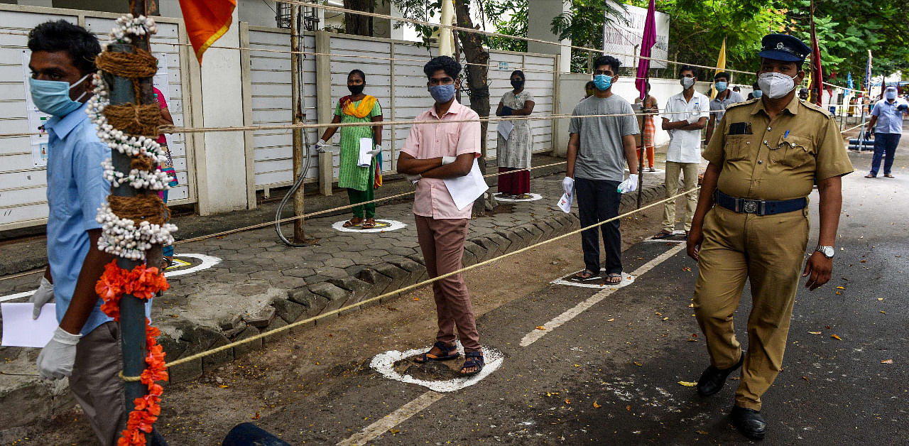 A police personnel (R) walks past as students line up standing on social distancing marks on the ground before entering an examination centre to take the National Eligibility cum Entrance Test (NEET)-2020, one of the most competitive entrance exams for entry to top national Medical colleges, in Chennai. Credit: AFP Photo