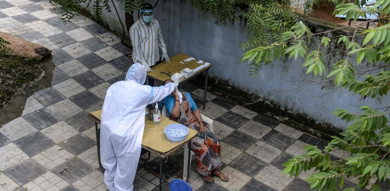 A health worker (L) wearing a Personal Protective Equipment (PPE) suit collects a swab sample from a woman for a Covid-19 test. Credit: AFP