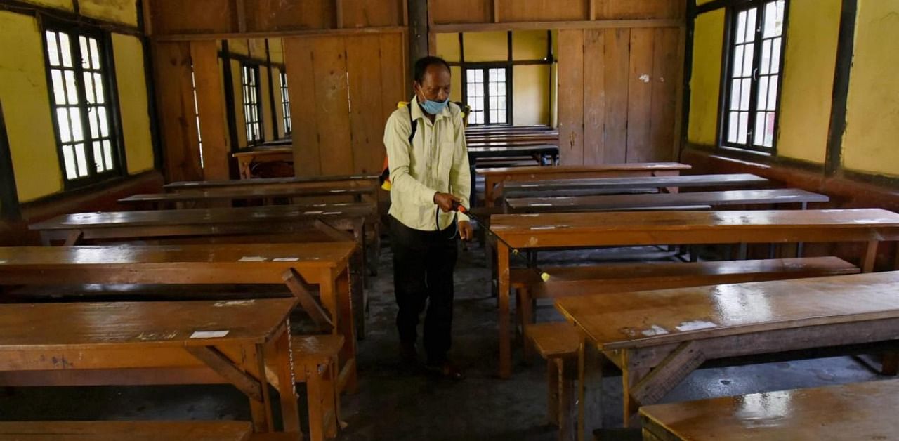 A staff member sprays disinfectant on benches ahead of the reopening of schools. Credit: PTI