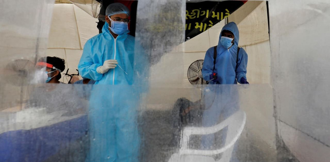 A healthcare worker wearing personal protective equipment (PPE) waits to take swabs from people for rapid antigen test alongside a road, amidst the coronavirus outbreak. Credit: Reuters