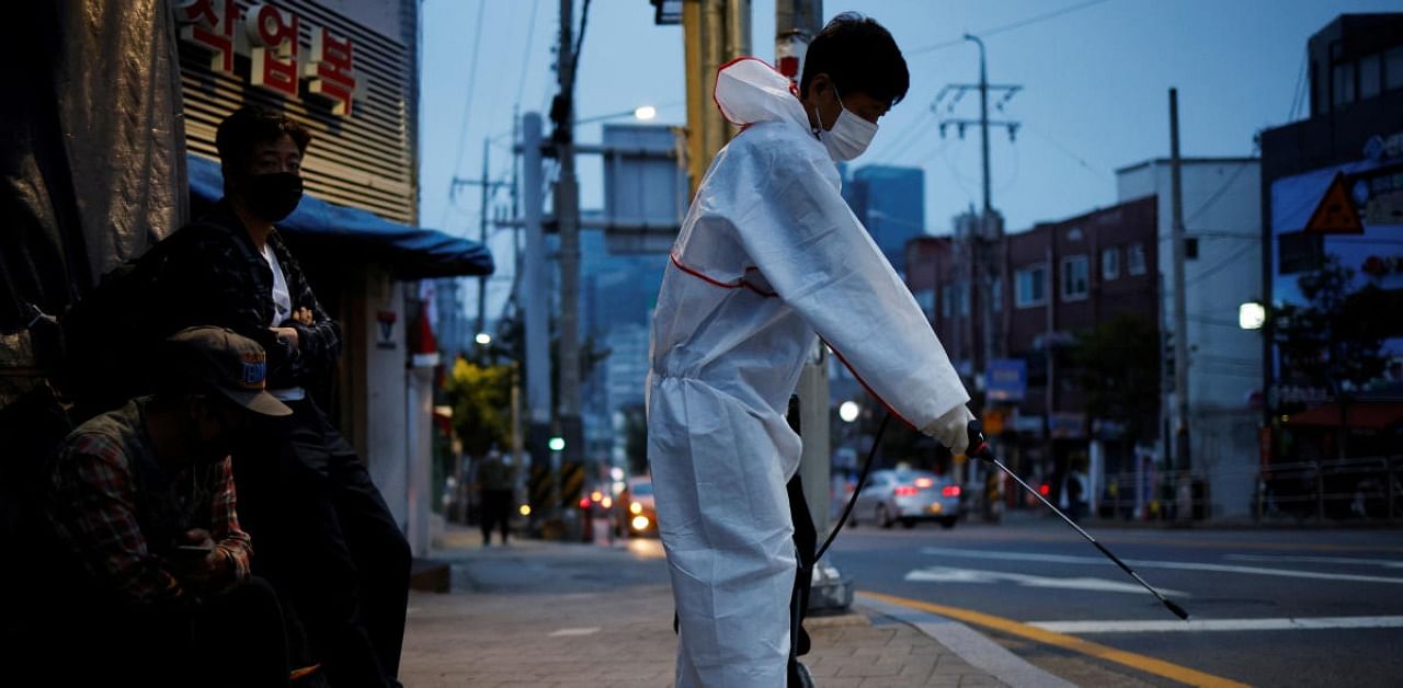 A government official sanitizes a street where day workers gathered to seek a job amid the coronavirus disease pandemic as day workers look on in Seoul, South Korea. Credit: Reuters
