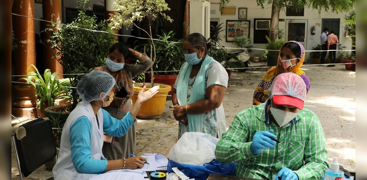 Health workers, left and right, take blood samples from local residents at a serological survey site in New Delhi, India. Credit: Bloomberg Photo