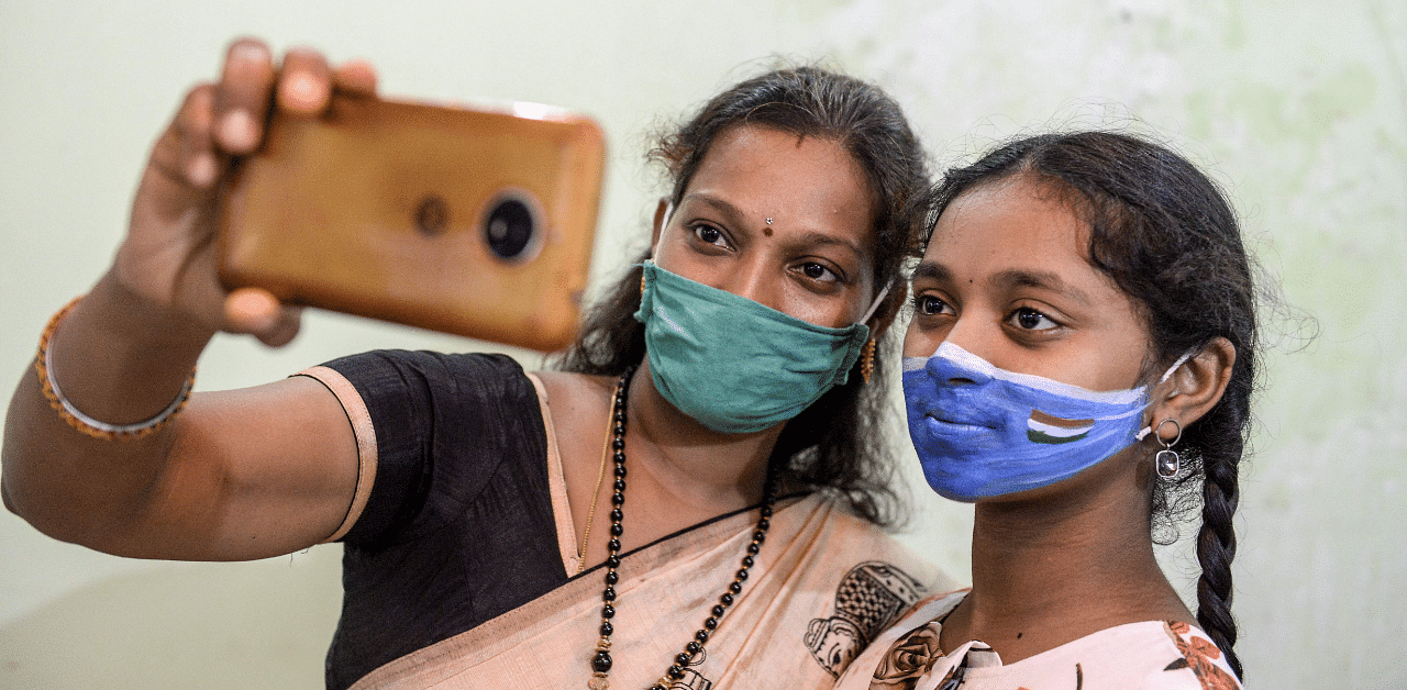 A woman (L) takes a selfie with her daughter who has a her face painted with a facemask by an artist to raise awareness about measures used to prevent the spread of the Covid-19. Credit: AFP Photo