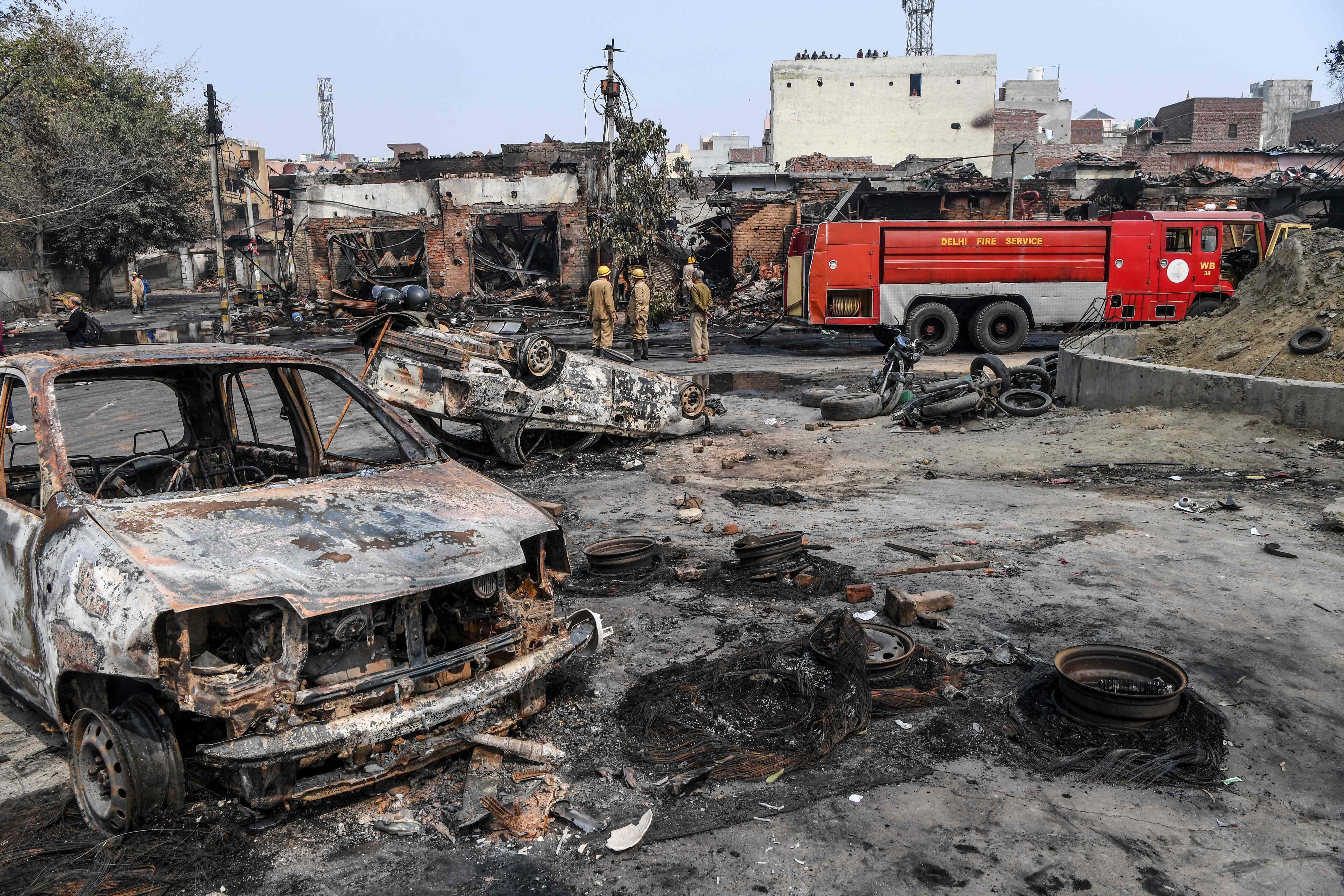 Firefighters stand near a fire rescue vehicle as they douse burnt-out tyre market premises following clashes between people supporting and opposing CAA, in New Delhi. Credits: AFP Photo