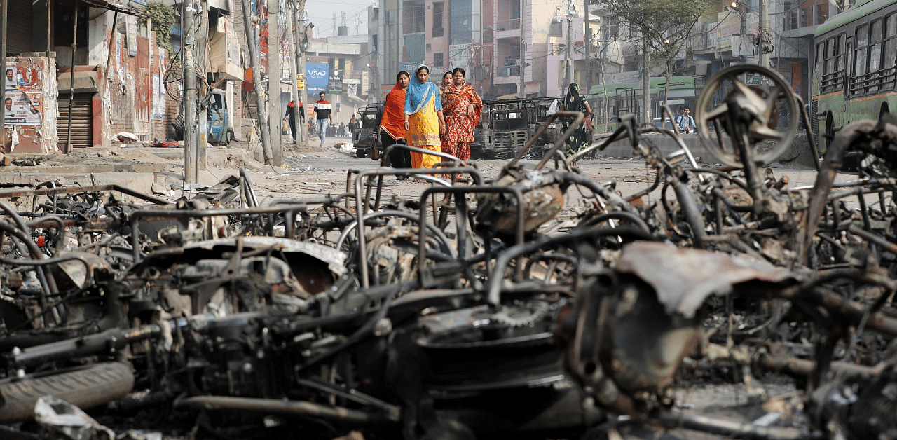 Women walk past charred vehicles in a riot affected area following clashes between people demonstrating for and against a new citizenship law in New Delhi, India, February 27. Credit: Reuters Photo