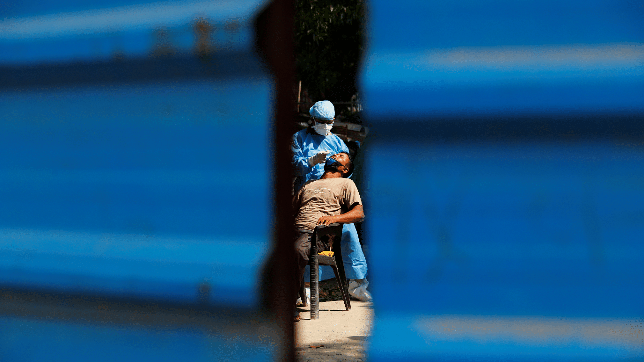 A healthcare worker wearing personal protective equipment (PPE) takes a swab from a migrant laborer. Credits: Reuters Photo