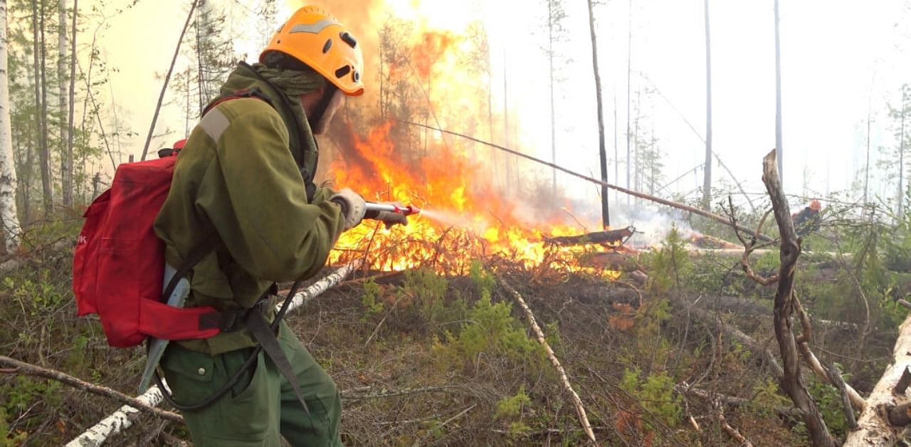 A specialist sprays water while extinguishing a forest fire in Krasnoyarsk region, Russia. Credit: Reuters