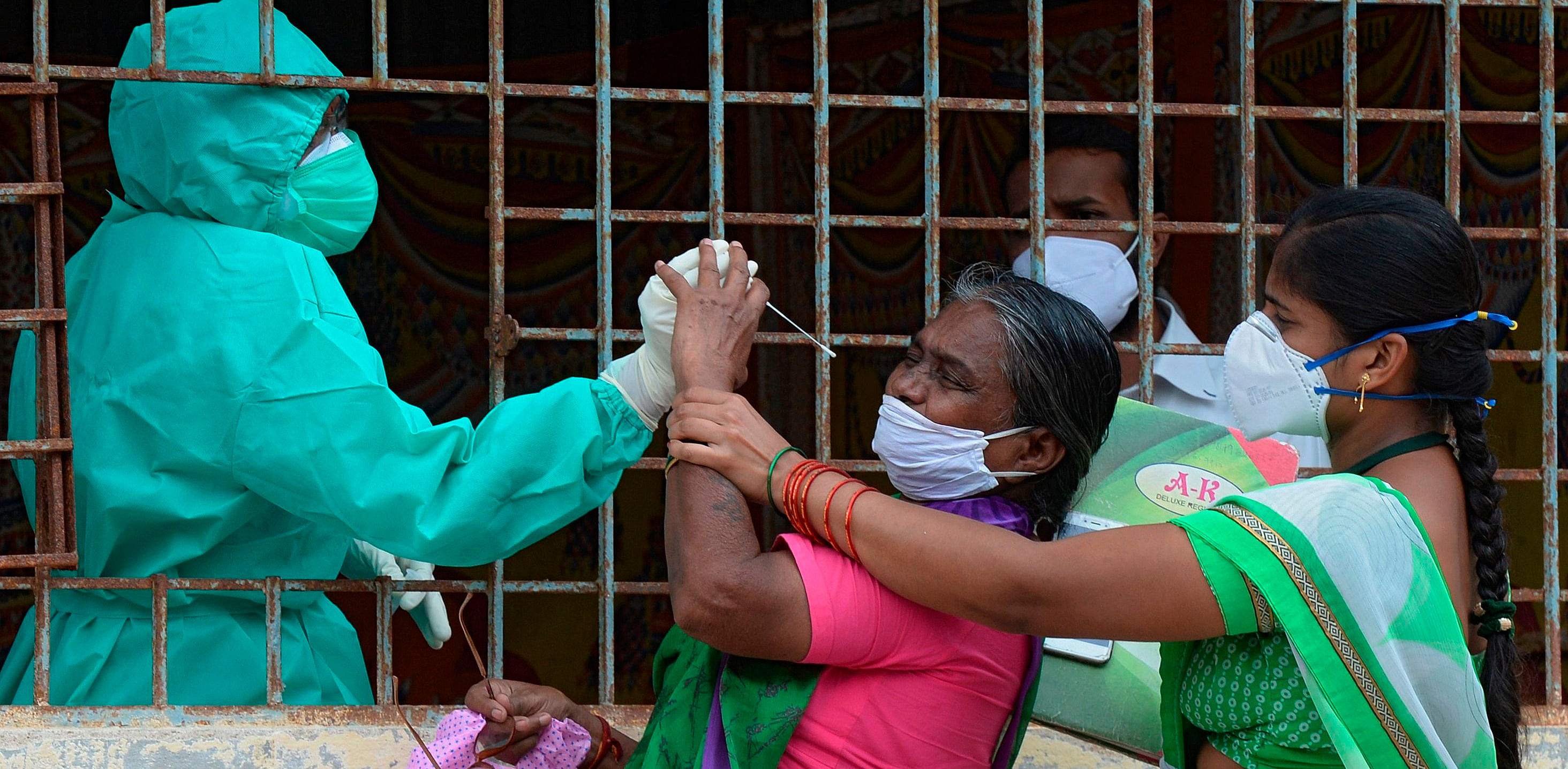 A woman (C) reacts as a health worker tries to collect her swab sample to test for the Covid-19 coronavirus at a slum area in Hyderabad. Credit: AFP