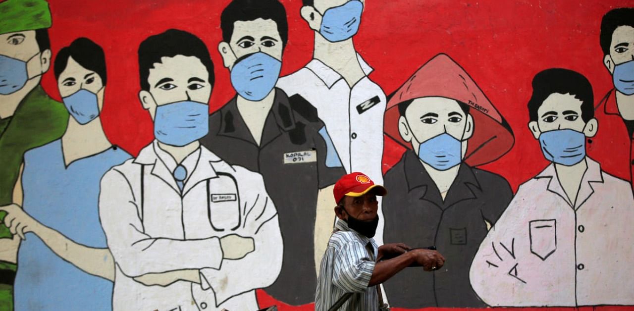 A man wearing a protective mask pulls a cart past a mural supporting frontline workers as the coronavirus disease outbreak continues in Jakarta, Indonesia. Credit: Reuters
