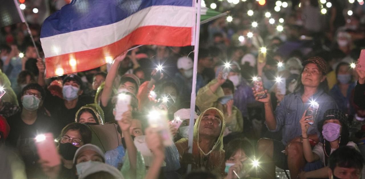 Pro-democracy protesters wave a flag and hold up lights during a protest at Sanam Luang in Bangkok, Thailand. Credit: AP