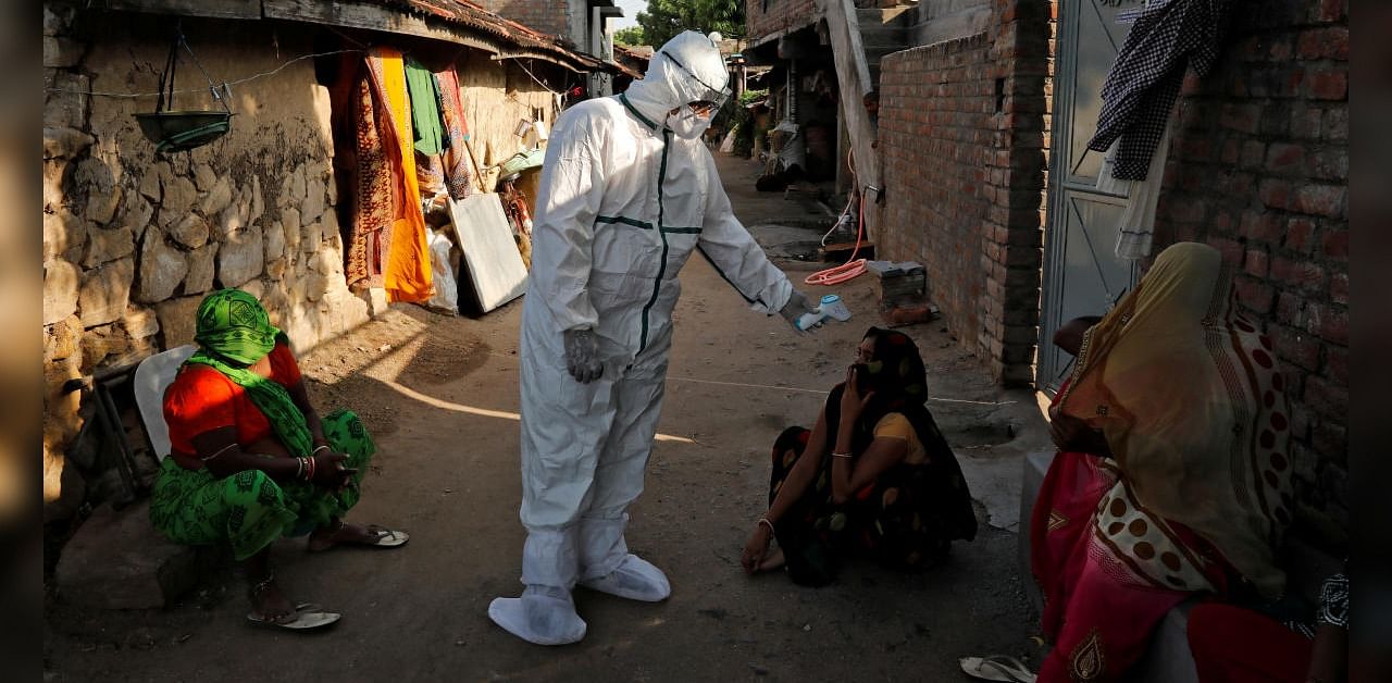 A healthcare worker wearing personal protective equipment (PPE) checks the temperature of a woman sitting outside her house in an alley during a door-to-door survey for the coronavirus disease (COVID-19), in Jakhan village in the western state of Gujarat, India, September 22, 2020. Credit: Reuters Photo
