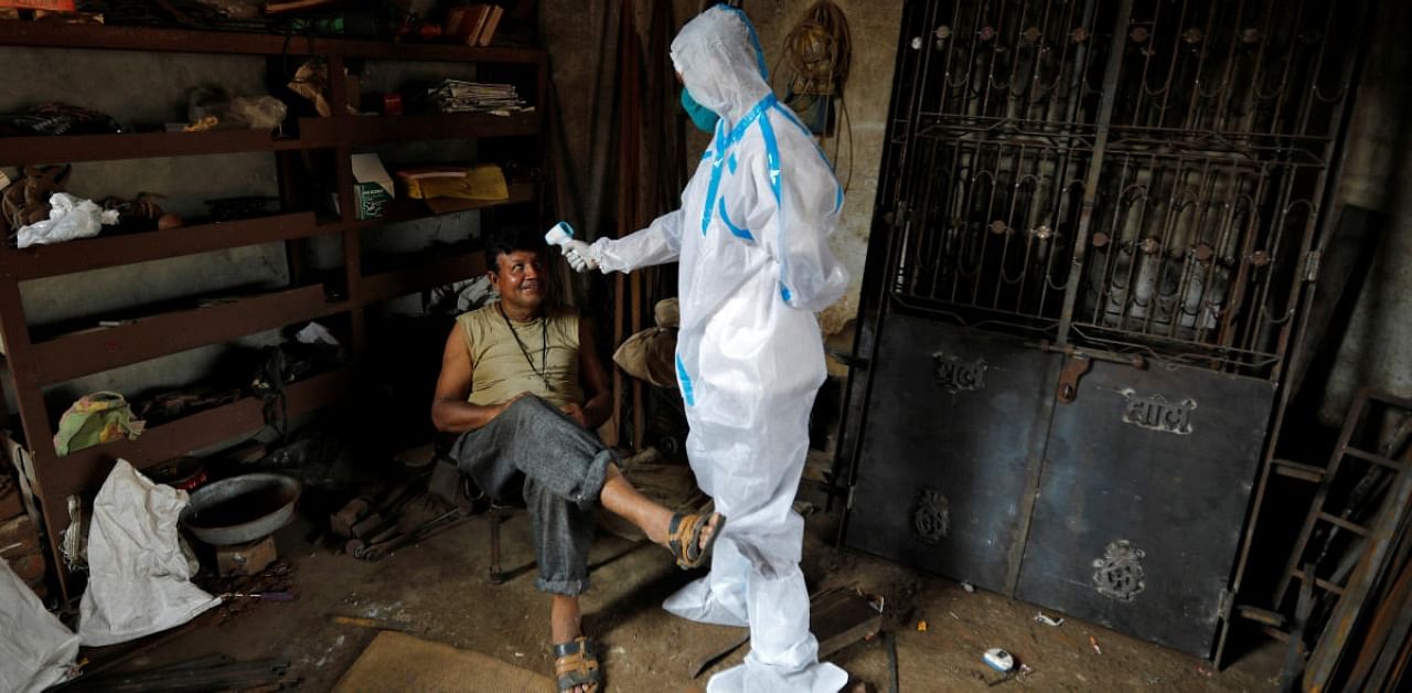 A healthcare worker wearing personal protective equipment (PPE) checks the temperature of a man inside his workshop during a door-to-door survey for the coronavirus disease. Credit: Reuters