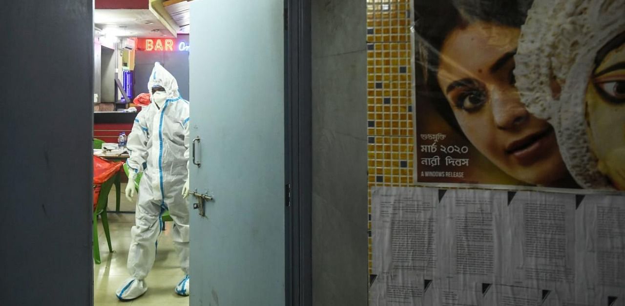 A health worker wearing a personal protective equipment (PPE) suit prepares to collect swab samples from people to test for the Covid-19 coronavirus, inside a single screen cinema hall building, as a poster of a Bengali cinema movie is seen pasted on the wall, in Kolkata. Credit: AFP