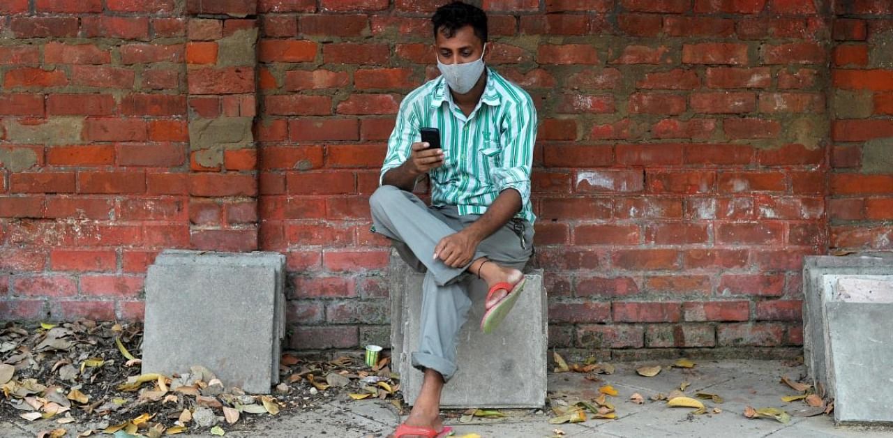 A man wearing a facemask as a preventive measure against the coronavirus, checks his mobile phone along the roadside. Credit: AFP