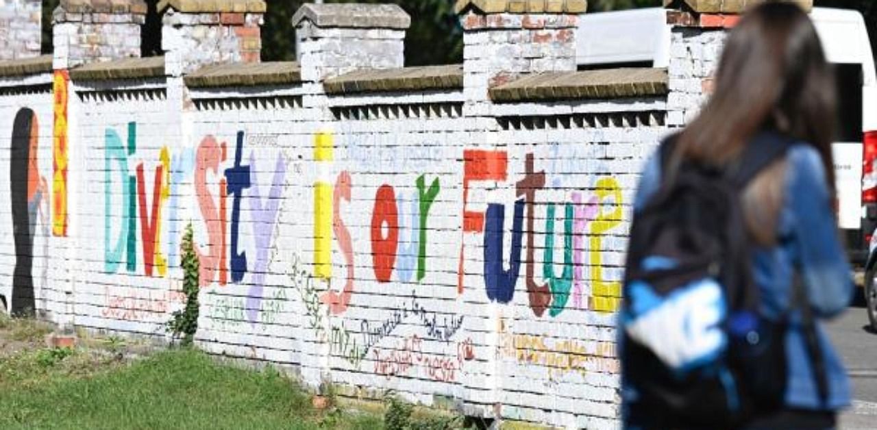  young woman stands in a public garden with graffitis on a wall reading "diversity is for the future" in Neuruppin, Eastern Germany. Credit: AFP Photo