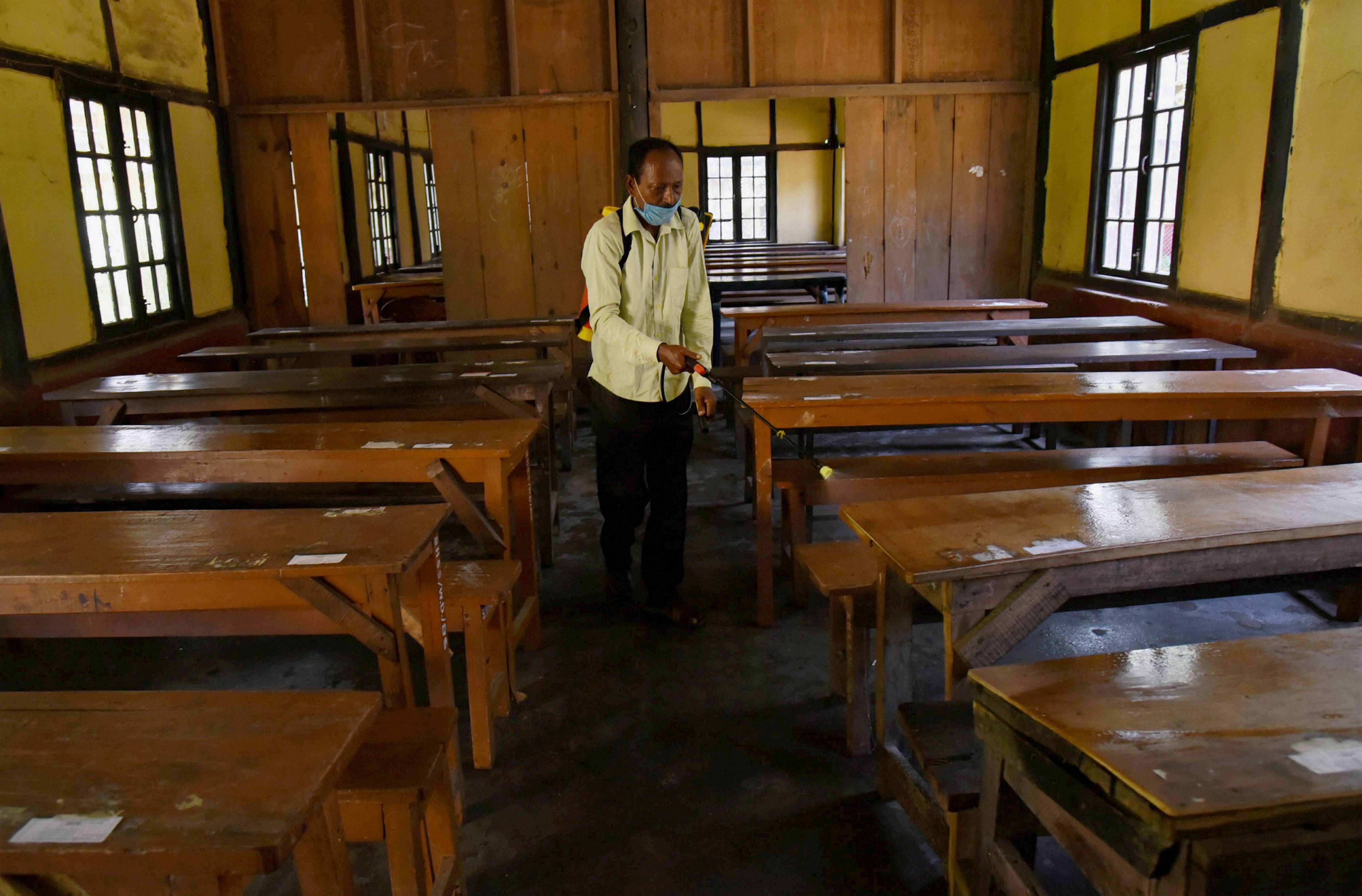 A staff member sprays disinfectant on benches ahead of the reopening of schools in Guwahati. Credit: PTI