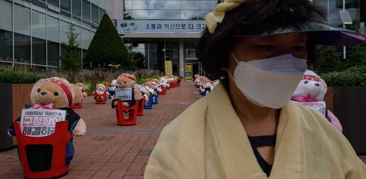 A protester sits in front of teddy bears dressed as protesters in order to comply with COVID-19 coronavirus rules against large public gatherings, during a protest by street vendors against a crackdown on unlicensed stalls, outside a district council office in Seoul. Credit: AFP Photo
