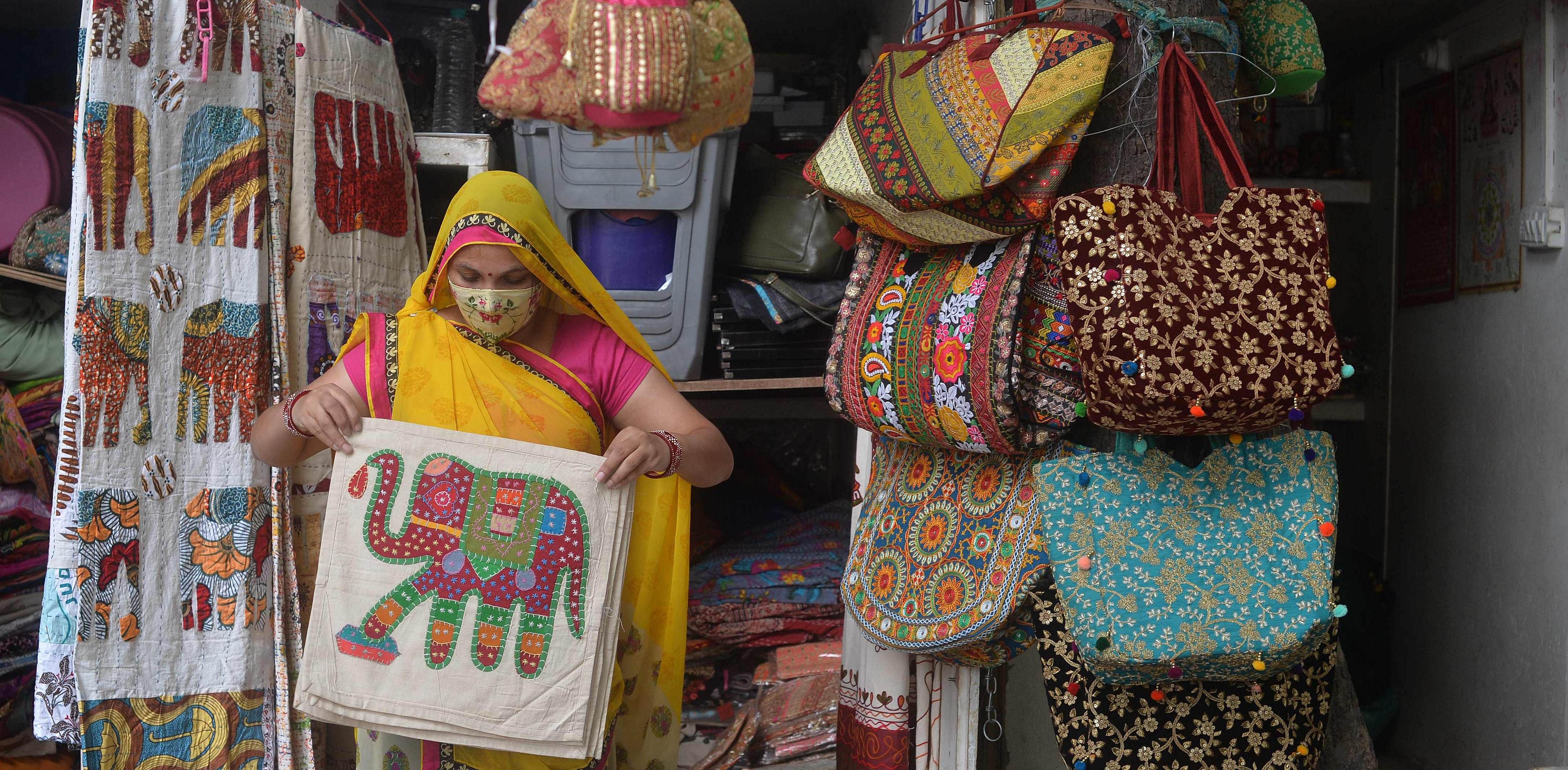 A woman vendor wearing a facemask as a preventive measure against the Covid-19 coronavirus, arranges cushion covers at her roadside shop in New Delhi. Credit: AFP