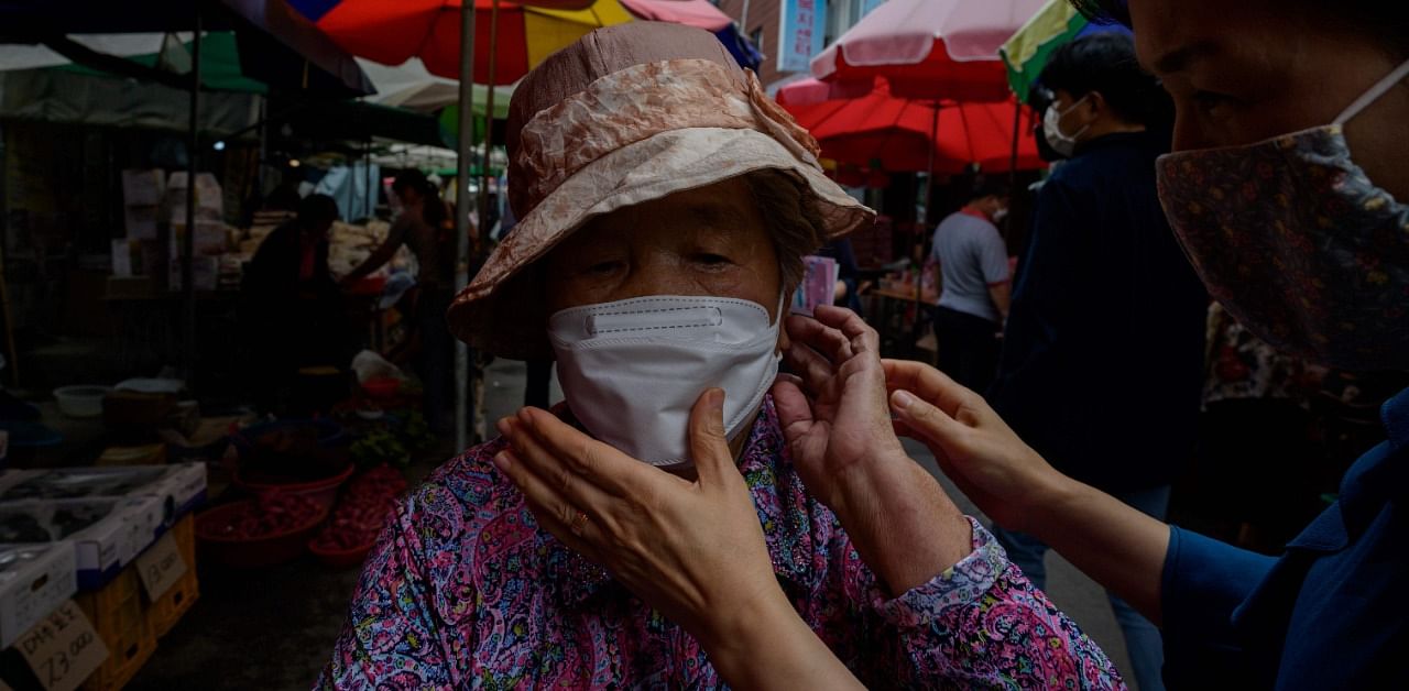 A volunteer handing out face masks helps an elderly woman change her face mask at at a market in Wanju. Credit: AFP Photo