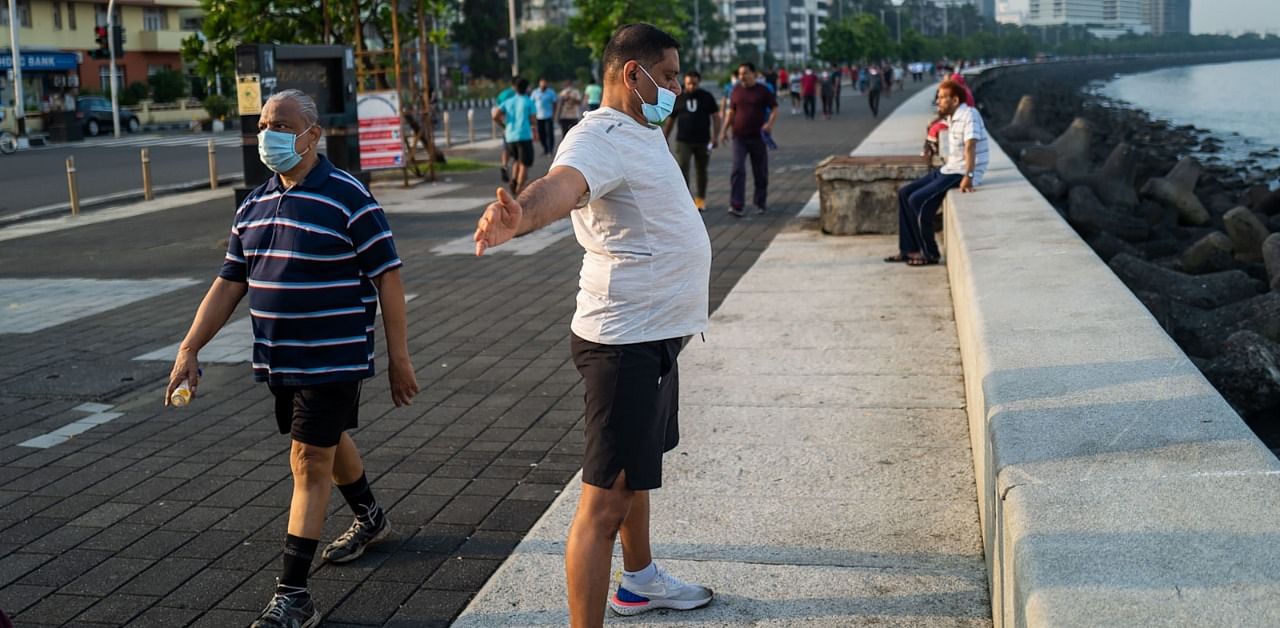 A man wearing a facemask as a preventive measure against the coronavirus does yoga as others walk along the Marine Drive waterfront in Mumbai. Credit: AFP Photo
