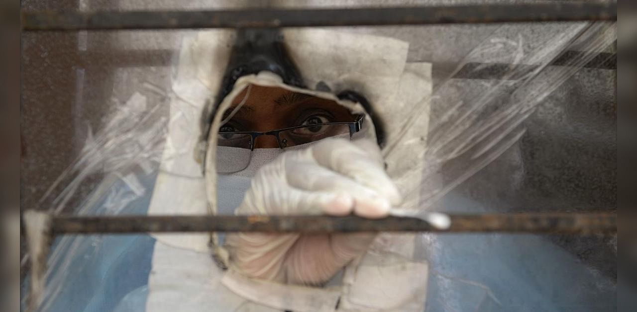 An Accredited Social Health Activist (ASHA) worker is seen through a plastic sheet as she waits to collect swab samples of residents to test for the Covid-19 coronavirus at a government primary health centre in Hyderabad on September 29, 2020. Credit: AFP Photo