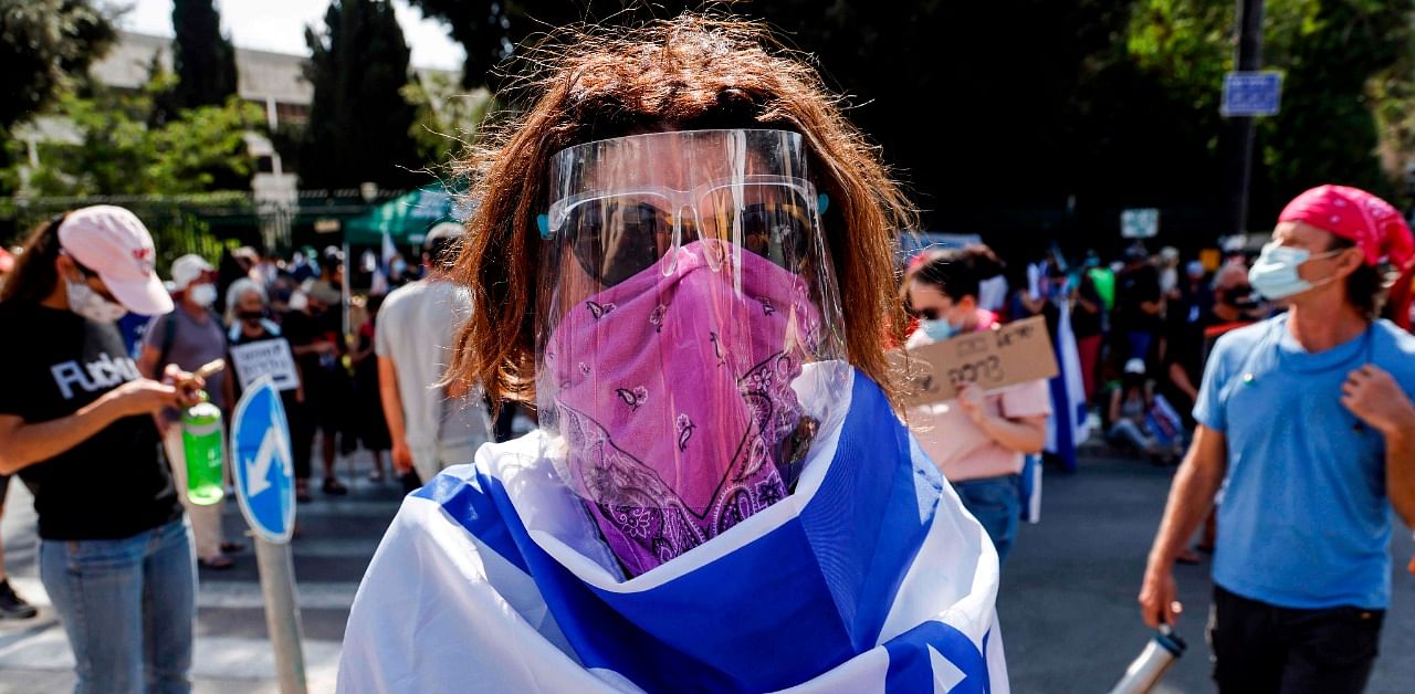 A woman, clad in mask and face shield due to the Covid-19 stands draped in an Israeli flag during a demonstration against the bill restricting protests. Credit: AFP Photo