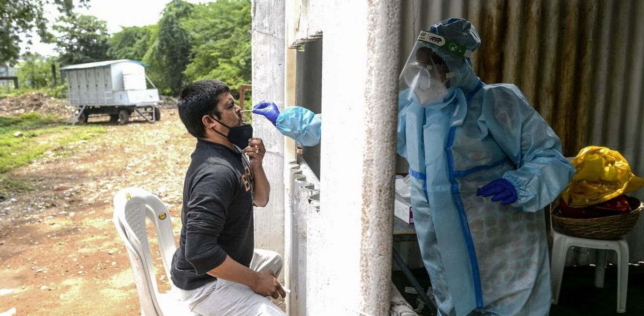 A health worker (R) wearing personal protective equipment (PPE) collects a swab sample from a resident for a coronavirus test at a temporarory collection centre. Credit: AFP