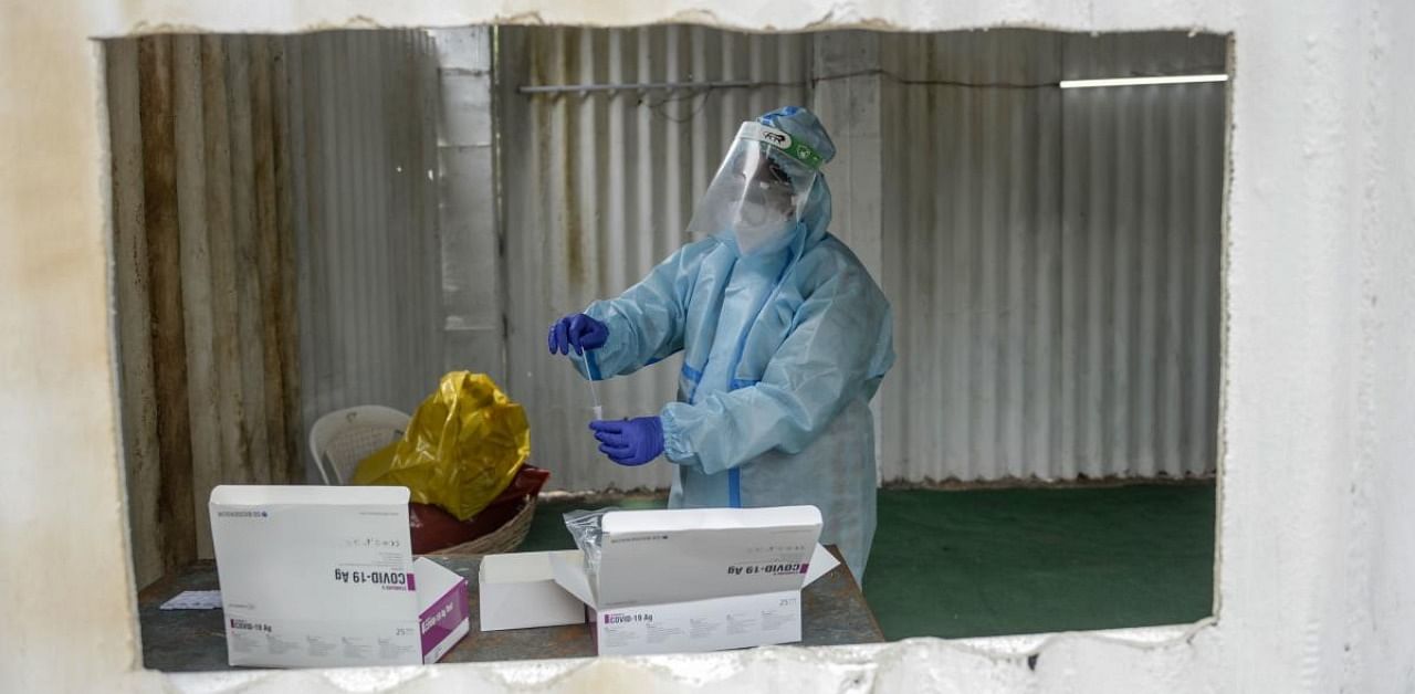 A health worker wearing personal protective equipment (PPE) checks on a swab sample from a resident for a coronavirus test at a temporarory collection centre. Credit: AFP