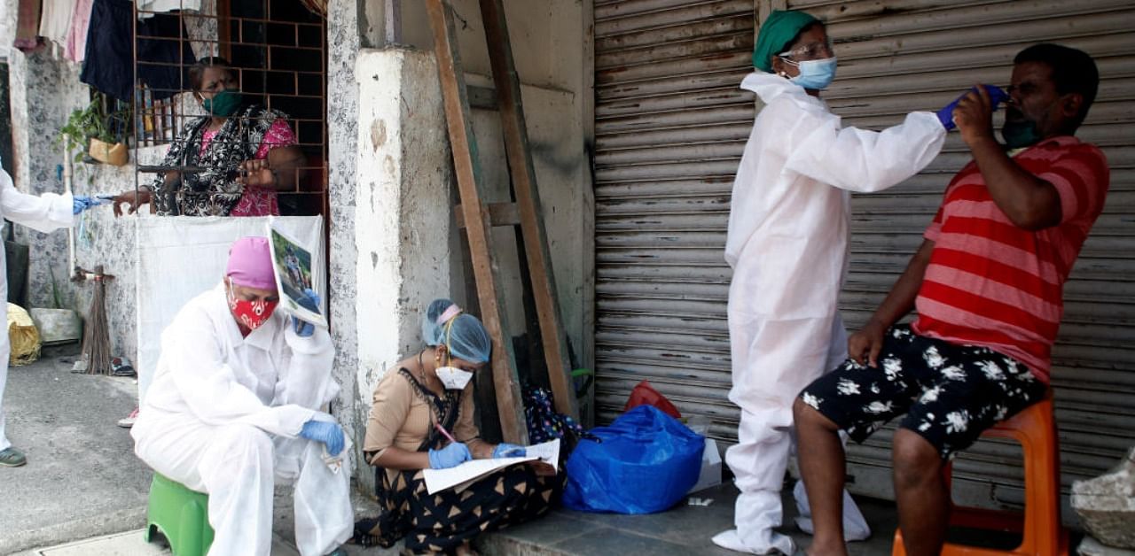 A health worker in personal protective equipment (PPE) rests as her colleagues test residents of a slum area during a check up campaign in Mumbai. Credit: Reuters