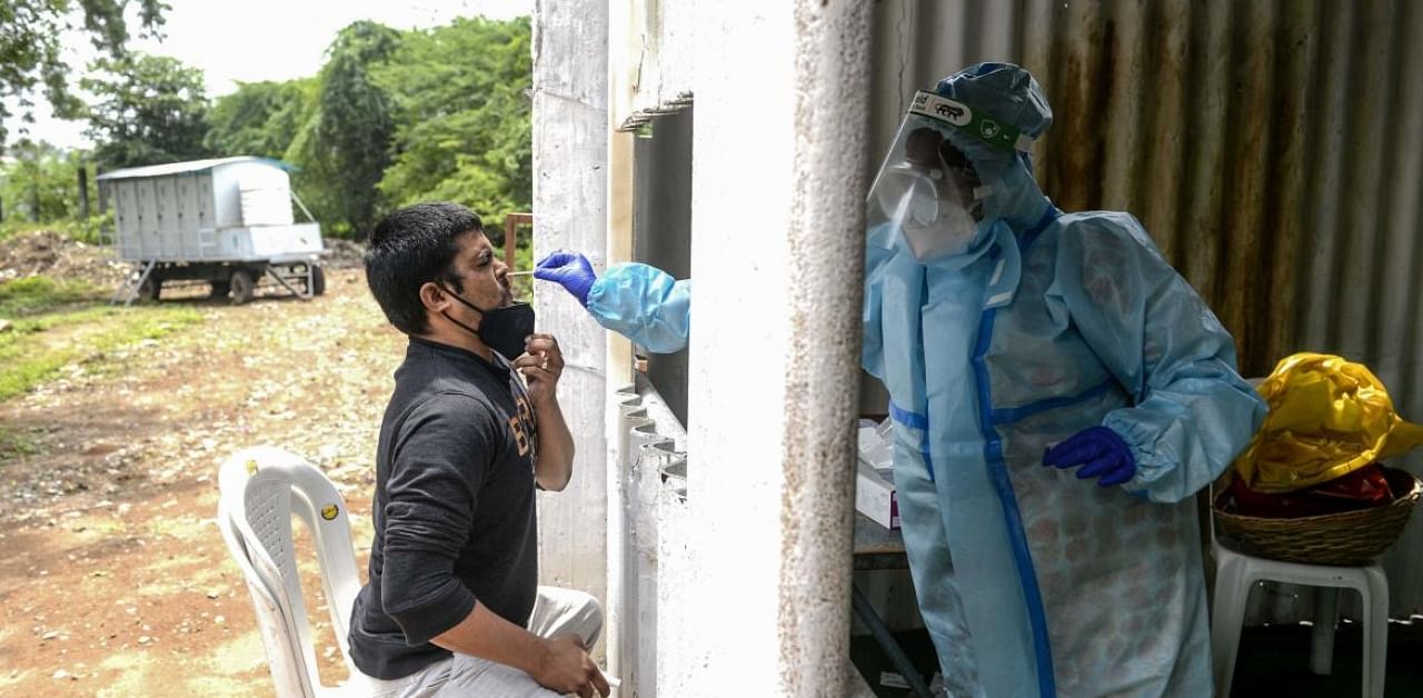 A health worker (R) wearing personal protective equipment (PPE) collects a swab sample from a resident for a Covid-19 coronavirus test at a collection centre in Secunderabad, the twin city of Hyderabad. Credit: AFP