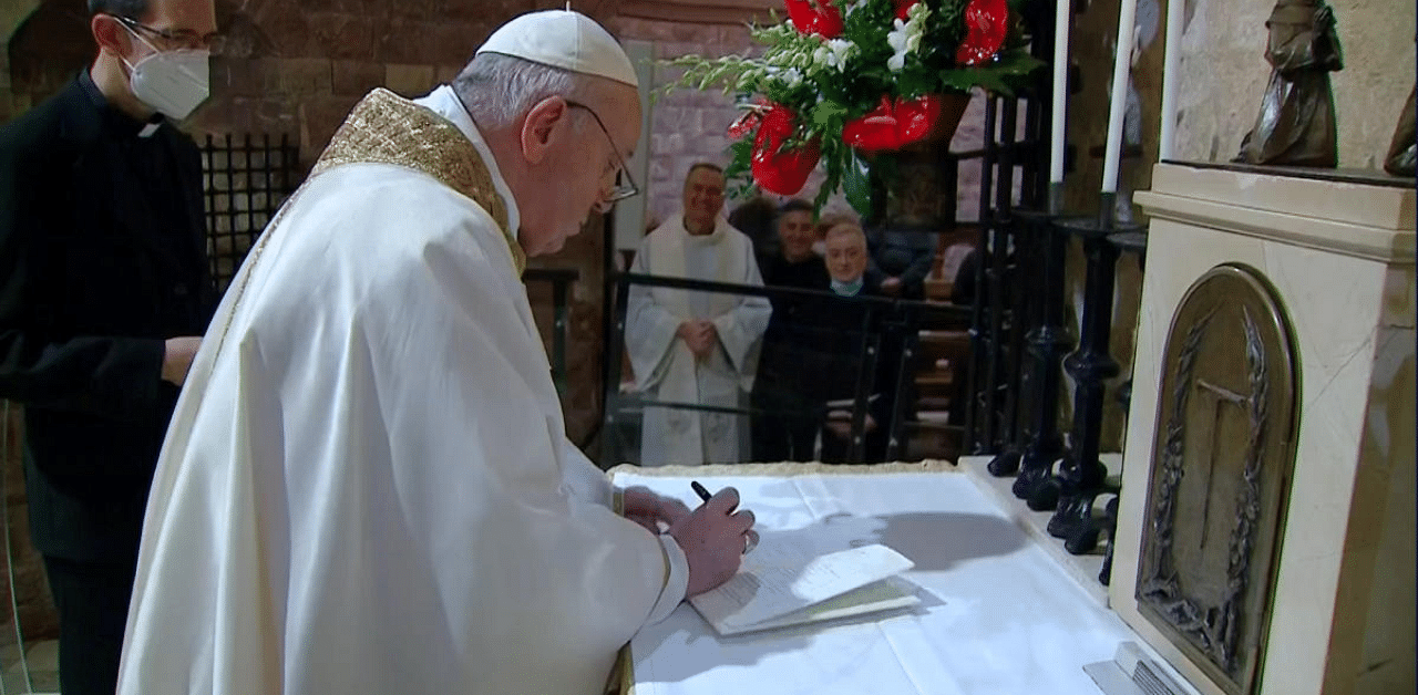 Pope Francis signs his latest encyclical, titled "Fratelli Tutti" (Brothers All), in the crypt where St. Francis of Assisi is buried in Assisi, Italy. Credit: Reuters Photo