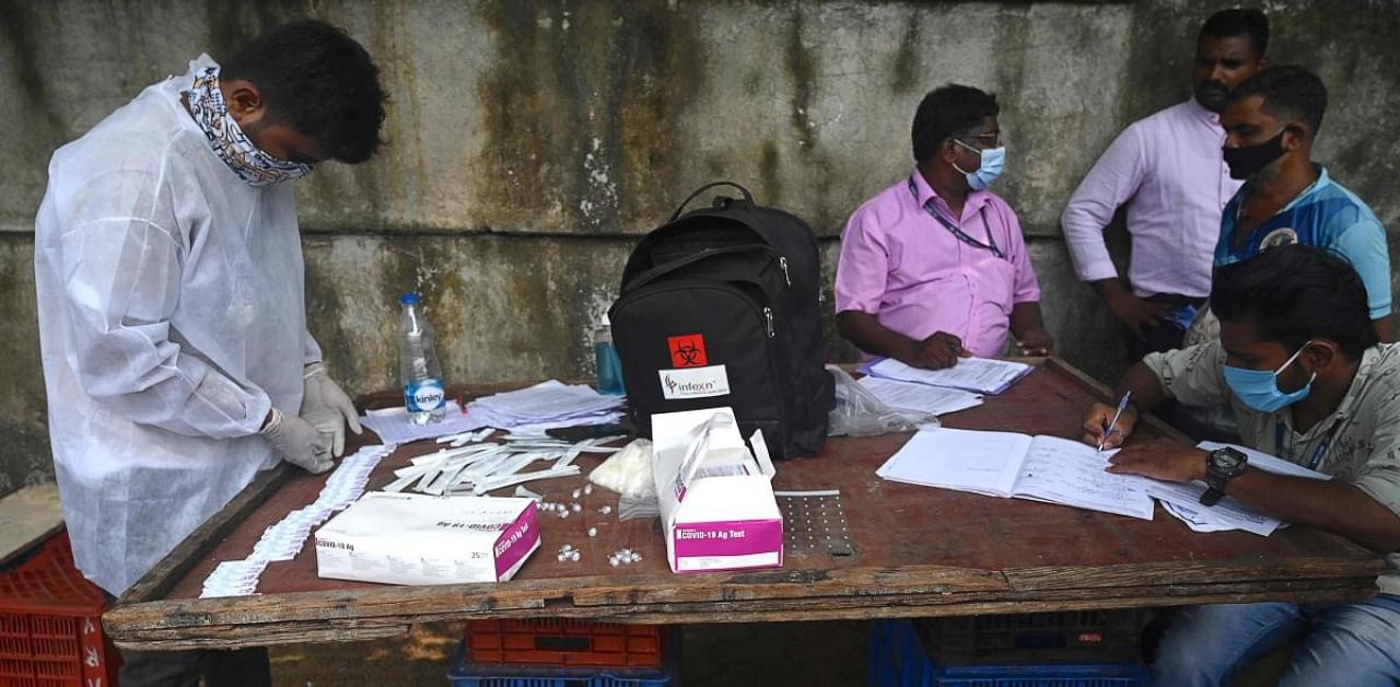 A health worker (L) checks swab samples collected during a medical screening for the Covid-19, in Mumbai. Credit: AFP