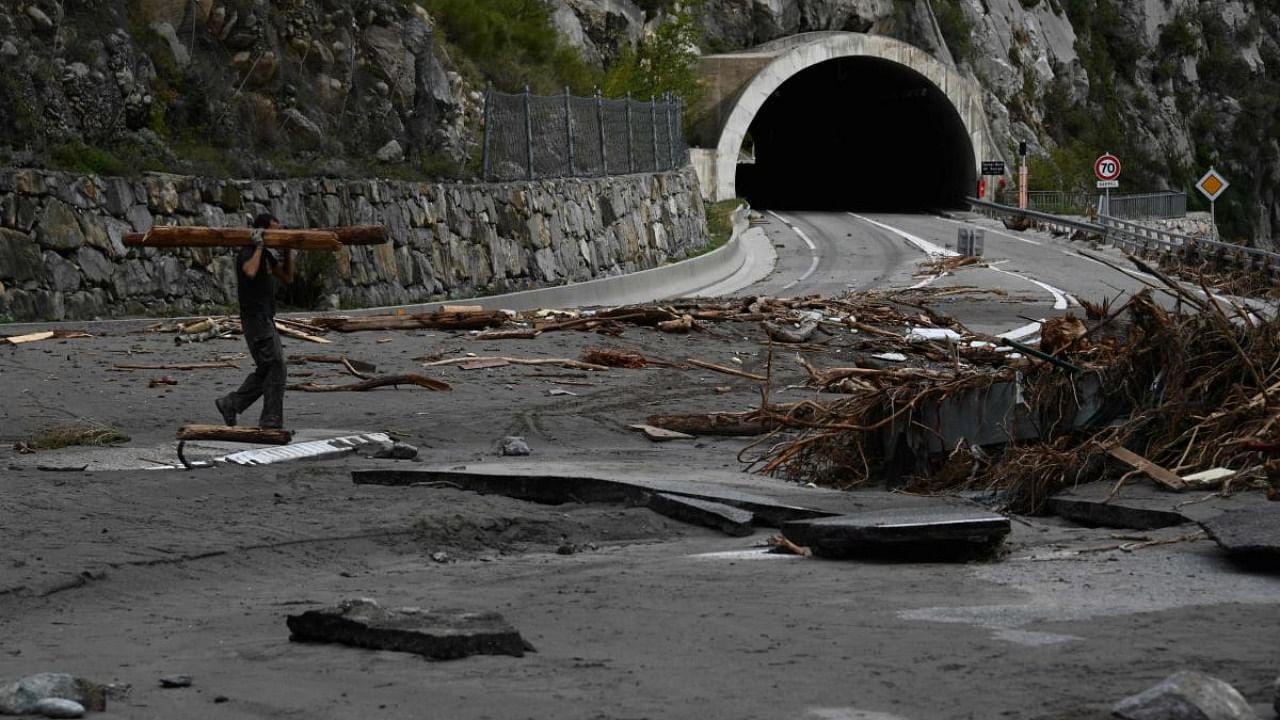 A man carries wood on October 6, 2020 on the damaged road leading to Breil-sur-Roya, a French village close to the Italian border, where houses were buried in mud and turned-over cars were stuck in the riverbed following heavy rains and floods. Credit: AFP.