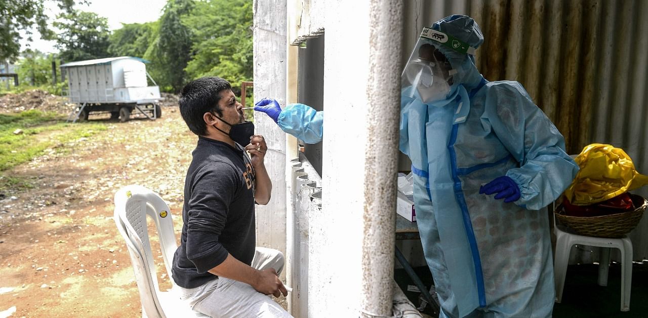 A health worker wearing PPE collects a swab sample from a resident for a Covid-19 test at a temporarory collection centre in Secunderabad, the twin city of Hyderabad. Credit: AFP Photo