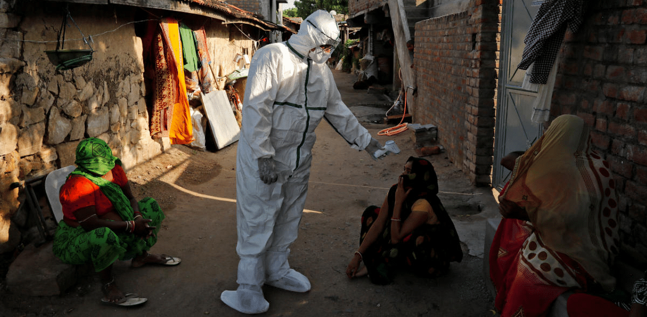 A healthcare worker wearing personal protective equipment (PPE) checks the temperature of a woman sitting outside her house in an alley during a door-to-door survey for the coronavirus disease, in Jakhan village. Credit: Reuters Photo