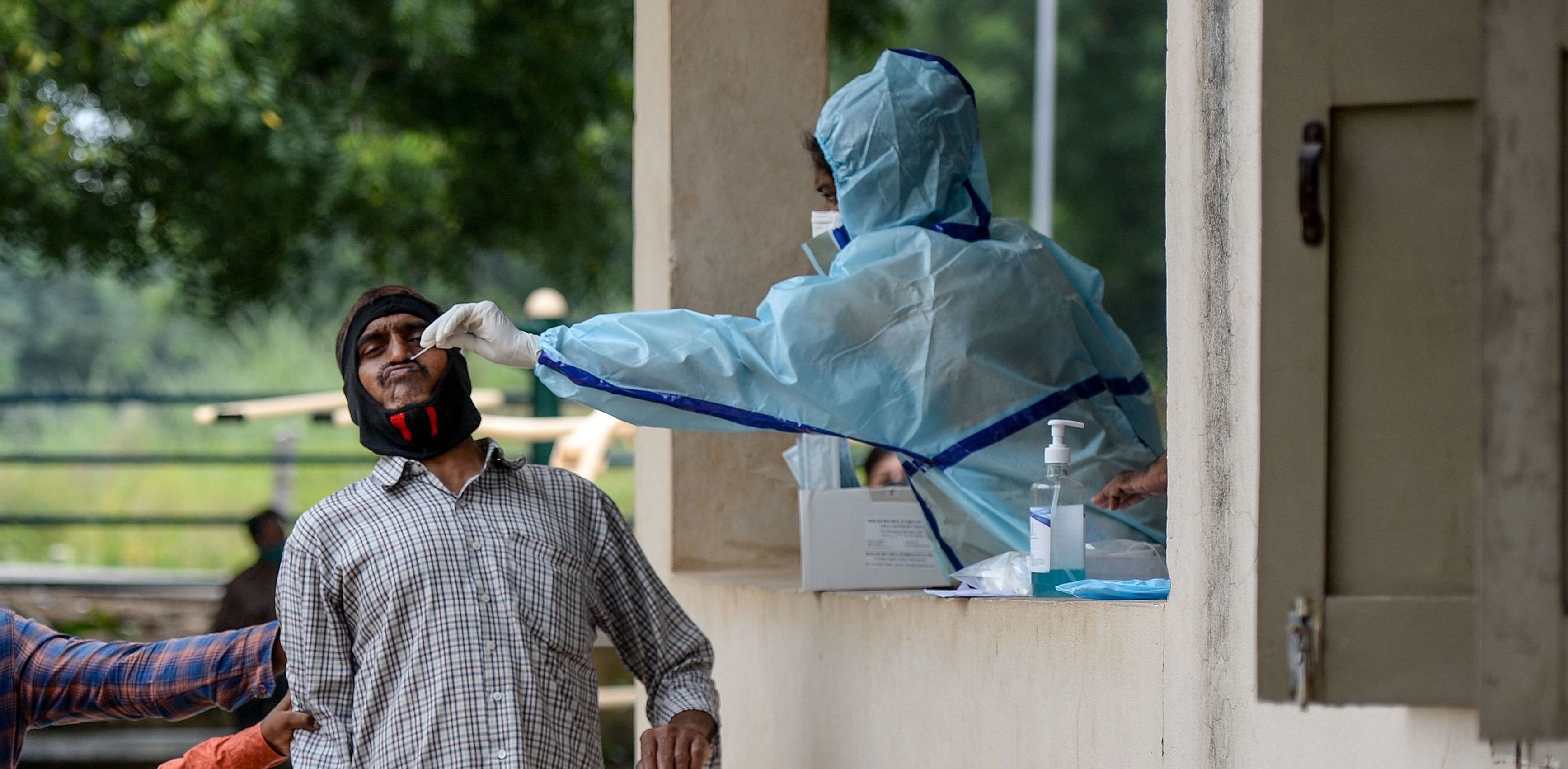 Residents hold a man as a health worker (R) collects a swab sample from him to test for the Covid-19 coronavirus at a community gym centre on the outskirts of Hyderabad. Credit: AFP