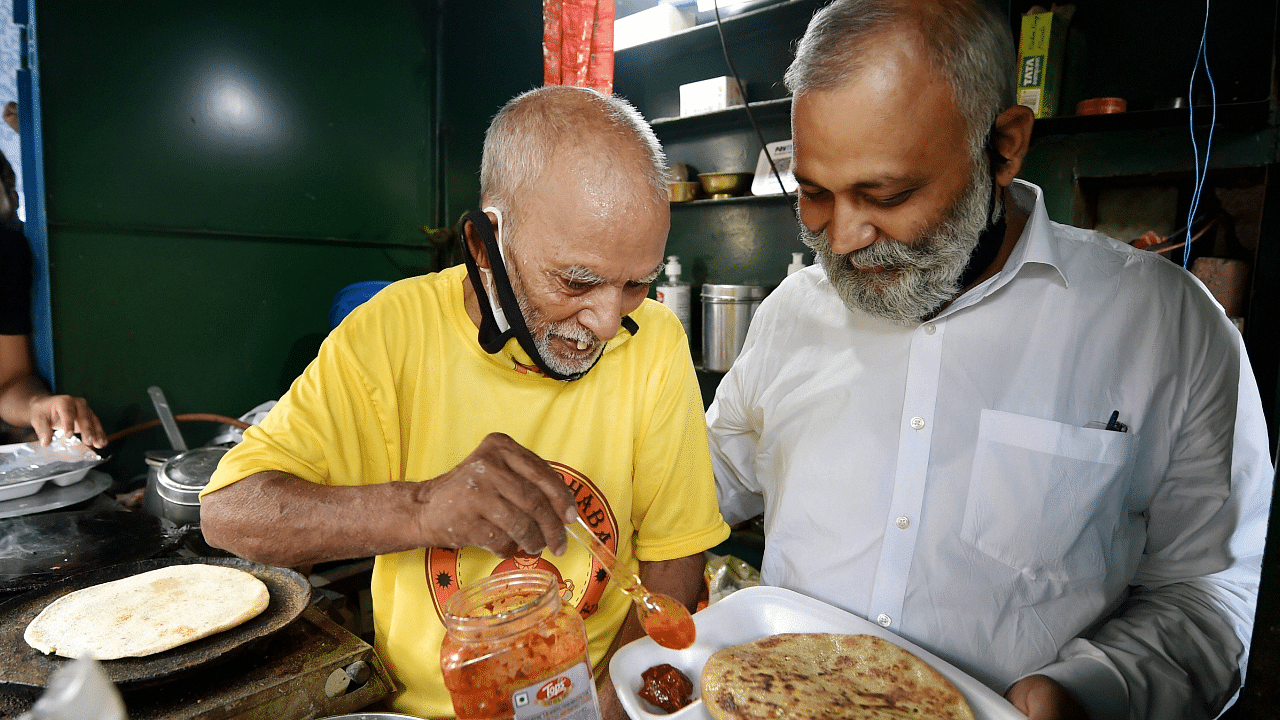 AAP MLA Somnath Bharti being served food by 80-year-old Kanta Prasad during the former's visit to 'Baba Ka Dhaba', at Malviya Nagar. Credits: PTI Photo