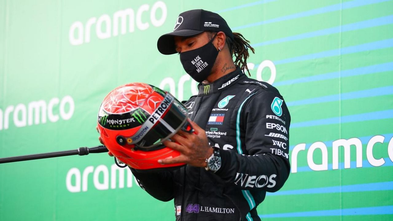 Winner Mercedes' British driver Lewis Hamilton holds the red helmet of former German Formula one champion Michael Schumacher that was offered to him by Mick Schumacher (unseen) on the podium after the German Formula One Eifel Grand Prix at the Nuerburgring circuit in Nuerburg. Credit: AFP.