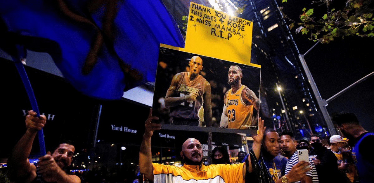 A Los Angeles Lakers fan holds a Kobe Bryant and LeBron James photo while watching on a TV at an outdoor restaurant during the 2020 NBA Finals between Los Angeles Lakers and Miami Heat. Credit: Reuters Photo