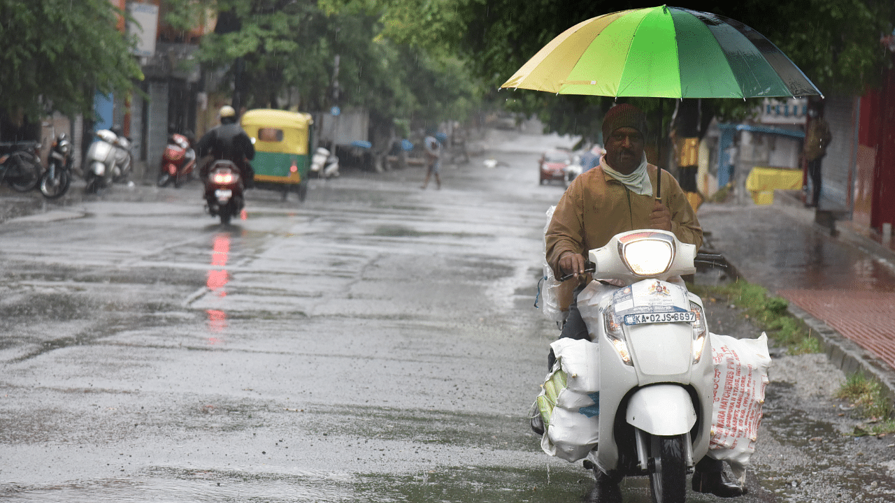 A man holding umbrella and run the two wheeler due to heavy rain in Karnataka. Credits: DH Photo