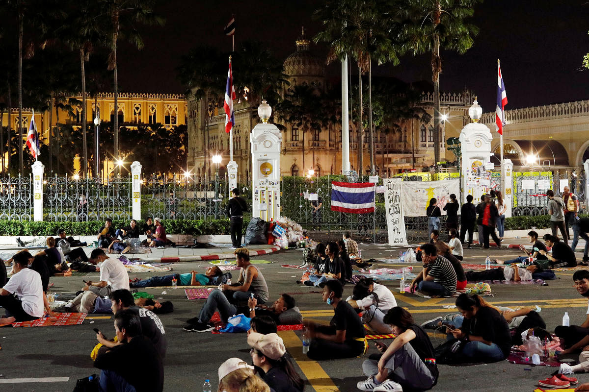 Pro-democracy demonstrators sit on the street outside the Government House during a Thai anti-government mass protest. Credit: Reuters