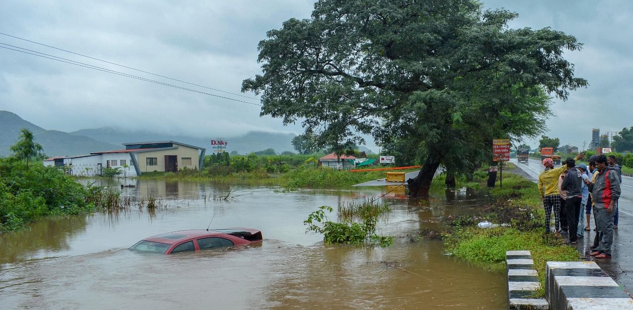 People look at a car almost submerged on a waterlogged service road along Pune-Bengalureu National Highway, following heavy rains. Credit: PTI Photo