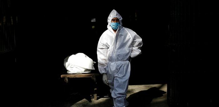 A health worker stands next to a body of a man who died due to the coronavirus. Credit: Reuters Photo