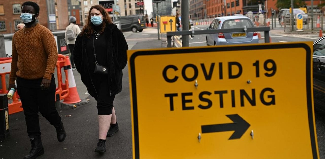 Pedestrians wearing protective face coverings walk past a Covid-19 testing sign in Manchester in north-west England. Credit: AFP.