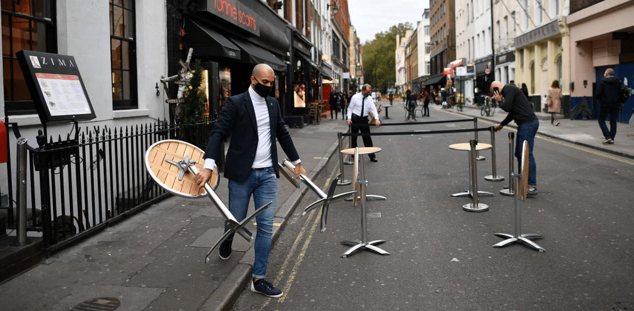 Employees place tables outside their restaurant in preparation for evening business in London as new restrictions on social gatherings and movement are set to come into force in London to combat the spread of the novel coronavirus. Credit: AFP Photo