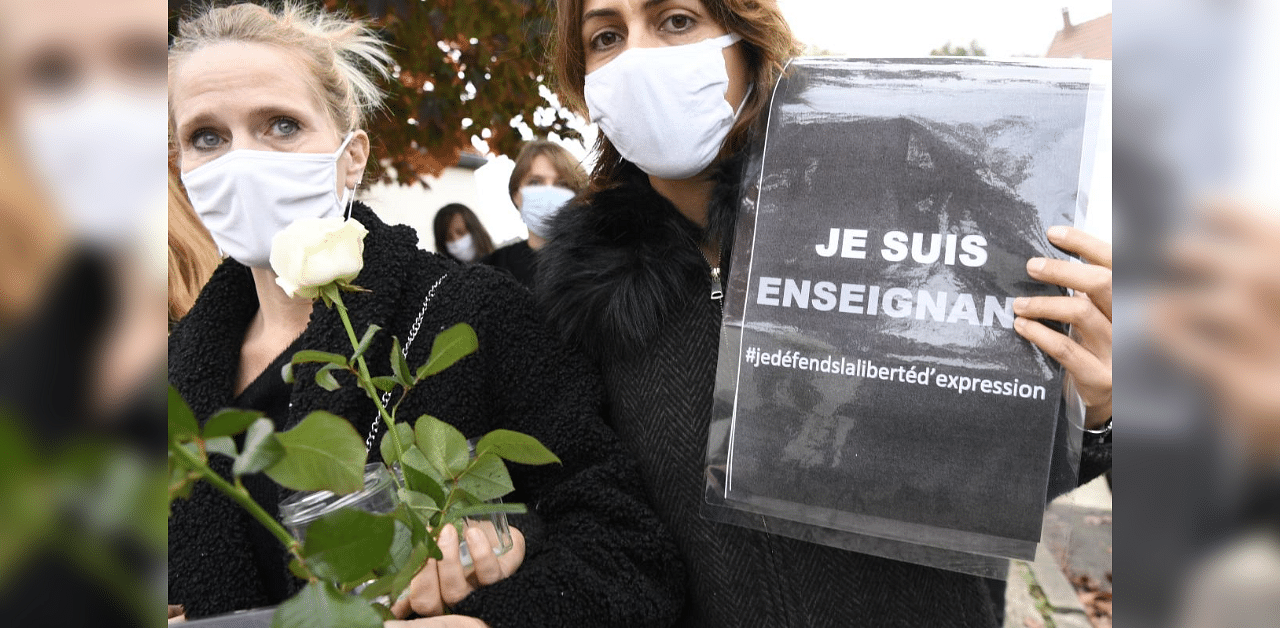 Women hold a sign reading 'I am a teacher - Freedom of speech' in front of a middle school in Conflans Saint-Honorine, 30kms northwest of Paris, on October 17, 2020, after a teacher was decapitated by an attacker who has been shot dead by policemen.  Credit: AFP Photo