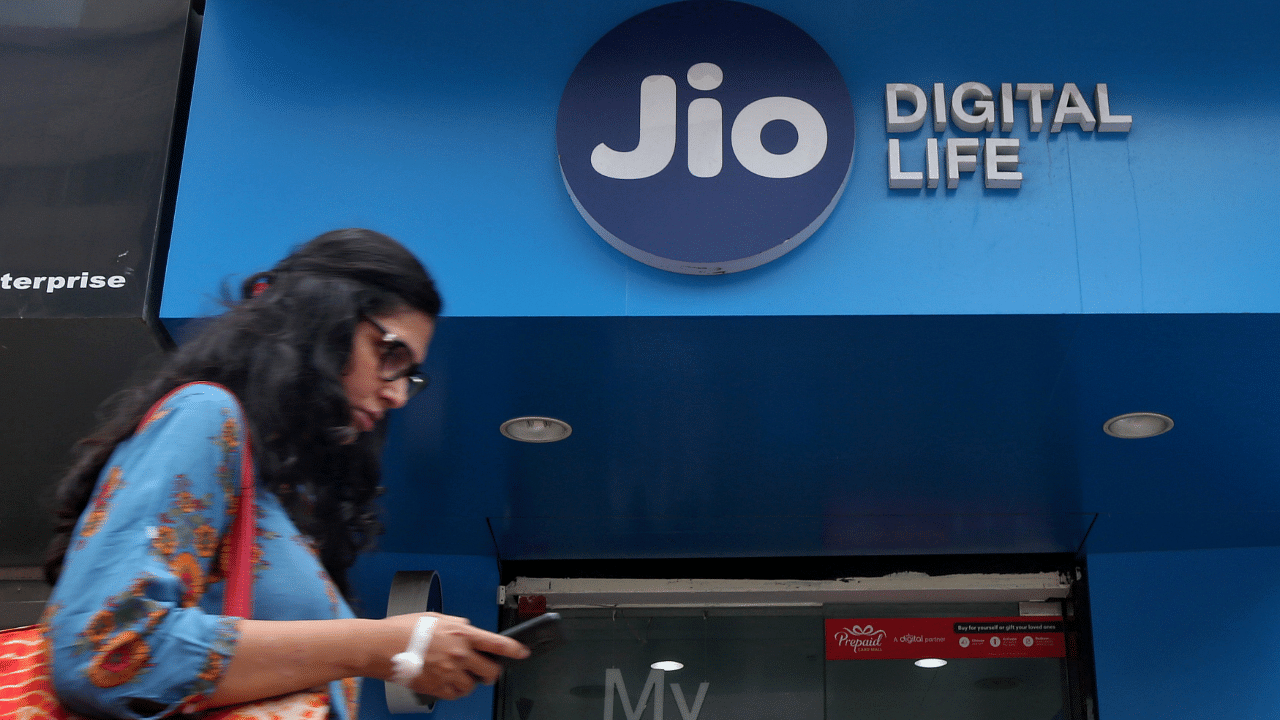 A woman checks her mobile phone as she walks past a mobile store of Reliance Industries' Jio telecoms. Credits: Reuters Photo