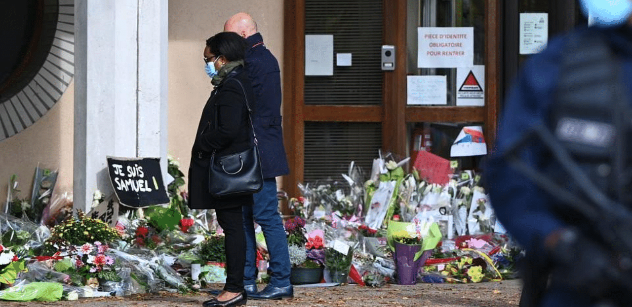 People look at flowers layed outside the Bois d'Aulne secondary school in homage to slain history teacher Samuel Paty, who was beheaded by an attacker for showing pupils cartoons of the Prophet Mohammed in his civics class, on October 19, 2020, in Conflans-Sainte-Honorine, northwest of Paris. Credit: AFP Photo