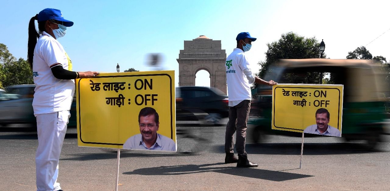 Civil defence volunteers hold placards on a busy road during an initiative taken by Delhi government asking commuters to switch-off the ignition of their vehicles at traffic red lights in order to control pollution levels. Credit: AFP Photo
