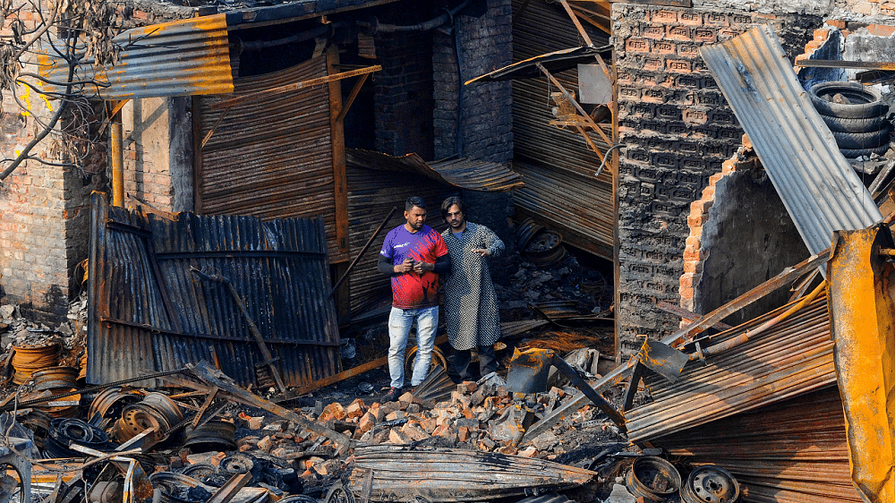 Shop owners look at the charred remains of the tyre market in riot affected Gokulpuri area of North East Delhi. Credits: PTI Photo